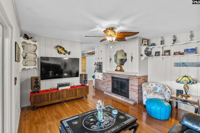 living room with a ceiling fan, a brick fireplace, and wood finished floors