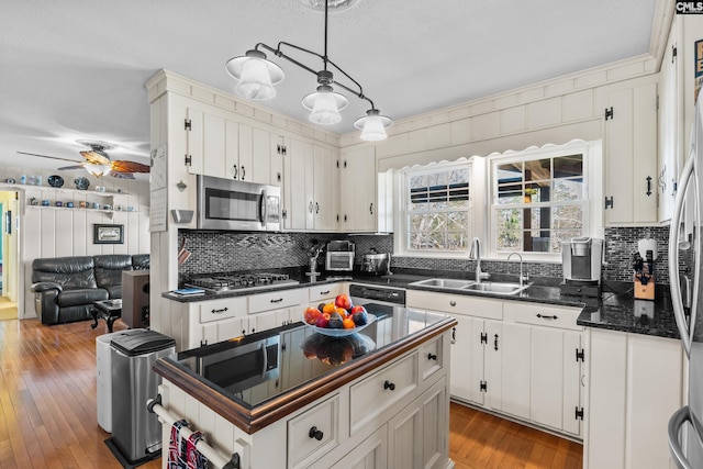 kitchen featuring a sink, stainless steel appliances, wood-type flooring, white cabinetry, and tasteful backsplash