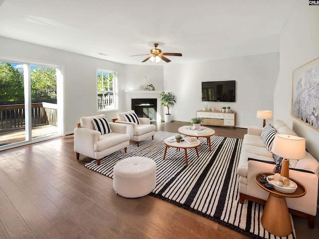 living area with a ceiling fan, a glass covered fireplace, wood finished floors, and visible vents