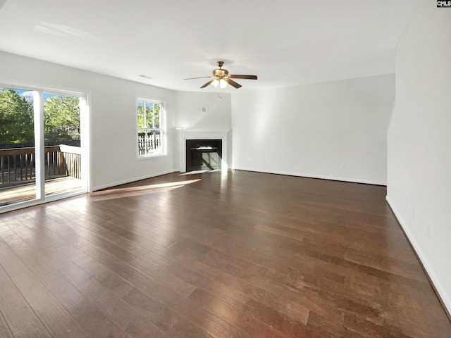 unfurnished living room with a glass covered fireplace, dark wood finished floors, baseboards, and ceiling fan