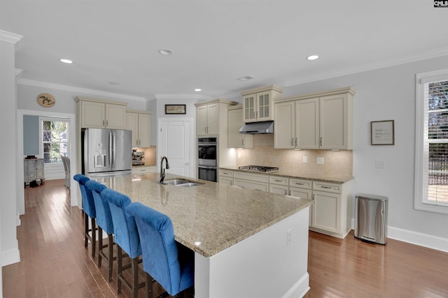 kitchen with under cabinet range hood, cream cabinetry, stainless steel appliances, and a sink