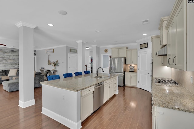 kitchen with visible vents, under cabinet range hood, open floor plan, stainless steel appliances, and a sink