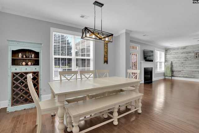 dining room featuring visible vents, a fireplace with flush hearth, wood finished floors, crown molding, and baseboards