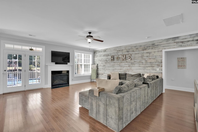 living area featuring a glass covered fireplace, baseboards, wood finished floors, and crown molding