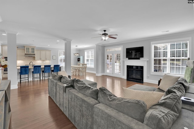 living area with a glass covered fireplace, visible vents, dark wood-style flooring, and ornamental molding