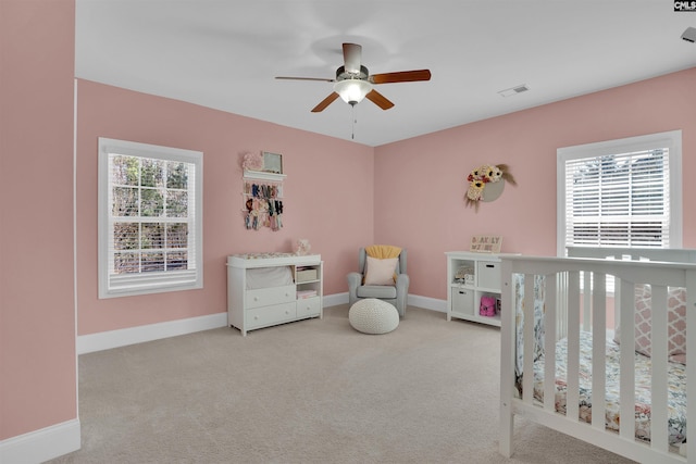 carpeted bedroom with a ceiling fan, multiple windows, baseboards, and visible vents