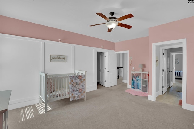 bedroom featuring a nursery area, a ceiling fan, baseboards, and carpet floors