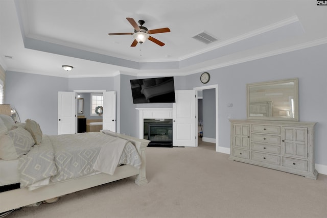 bedroom featuring visible vents, a tray ceiling, a glass covered fireplace, carpet floors, and baseboards