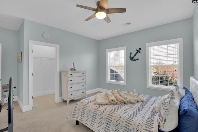 bedroom with visible vents, a walk in closet, a closet, baseboards, and light colored carpet