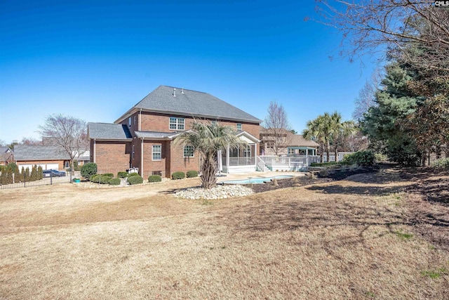 rear view of house with brick siding, a lawn, a sunroom, and fence