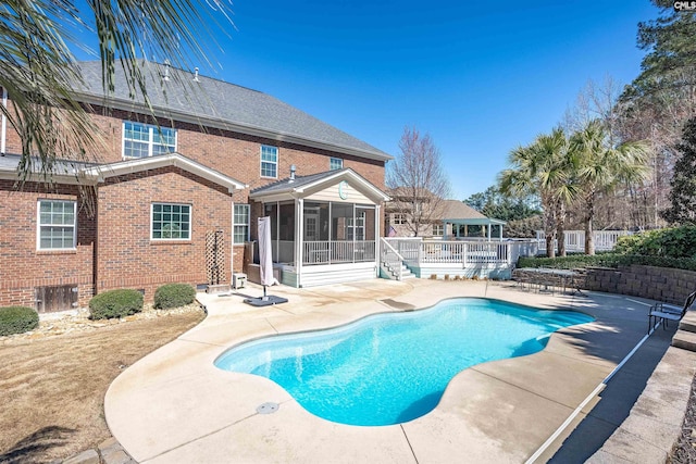 view of pool featuring fence, a fenced in pool, a wooden deck, a sunroom, and a patio area