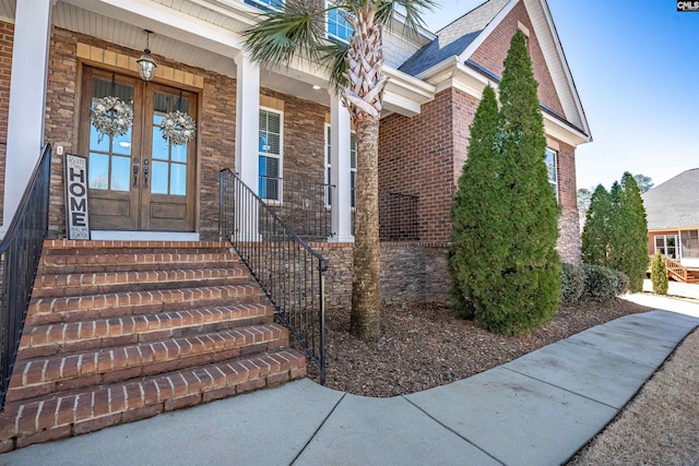 doorway to property featuring french doors, brick siding, and roof with shingles