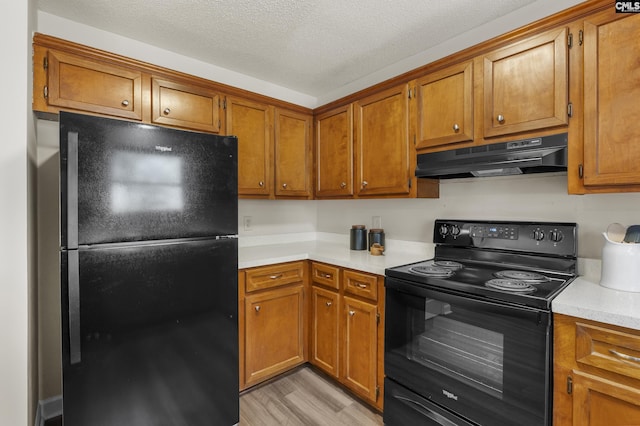 kitchen with brown cabinetry, black appliances, light countertops, under cabinet range hood, and a textured ceiling