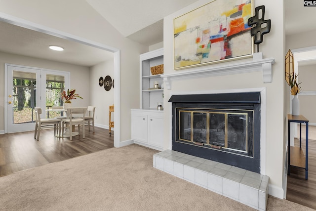 carpeted living area with a glass covered fireplace, wood finished floors, baseboards, and vaulted ceiling