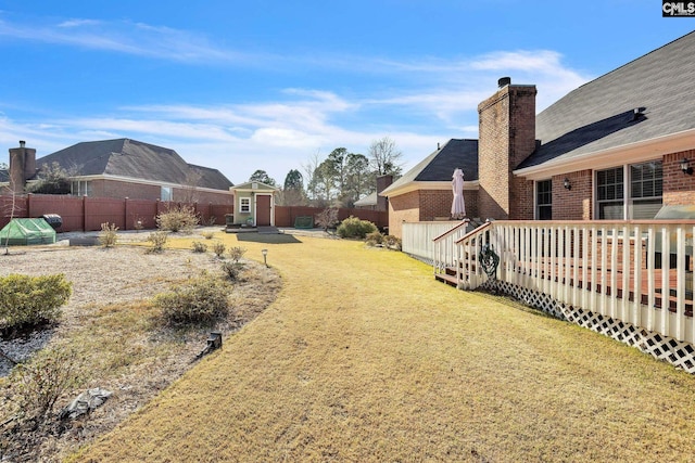 view of yard with an outbuilding, a deck, a storage shed, and a fenced backyard