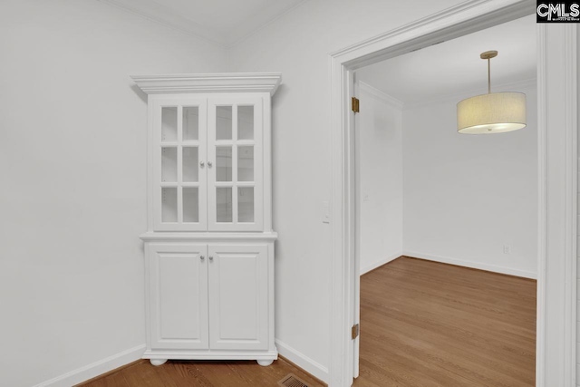 interior space featuring visible vents, wood finished floors, baseboards, and ornamental molding