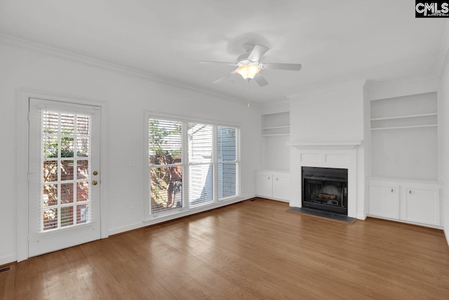 unfurnished living room with built in features, plenty of natural light, wood finished floors, and a fireplace