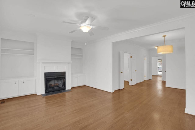 unfurnished living room with built in shelves, wood finished floors, a fireplace with flush hearth, ceiling fan, and crown molding