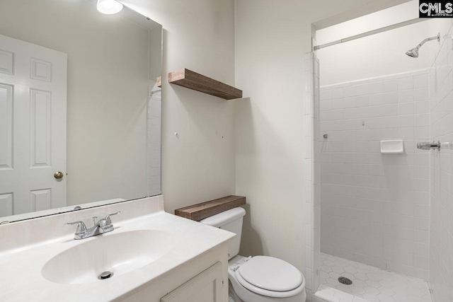 bathroom featuring a tile shower, toilet, and vanity