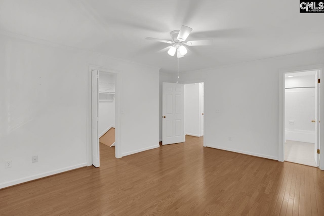 unfurnished bedroom with a spacious closet, wood finished floors, baseboards, and ensuite bathroom