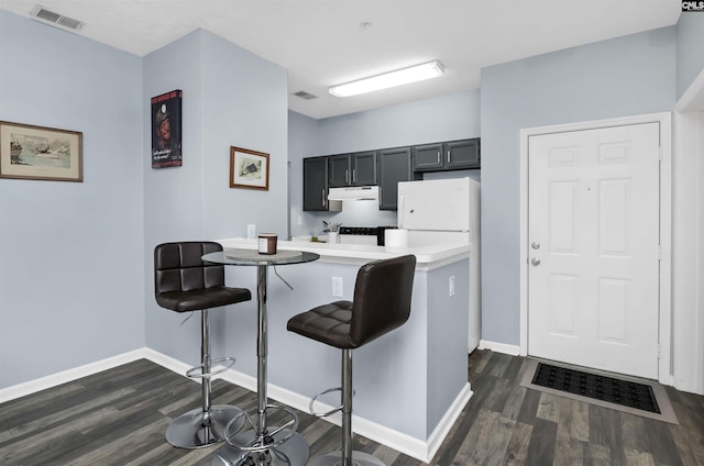 kitchen with visible vents, dark wood-type flooring, under cabinet range hood, a breakfast bar area, and a peninsula