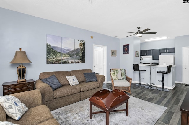 living room with dark wood-type flooring, a ceiling fan, and baseboards