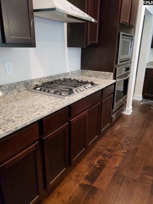 kitchen with light stone countertops, dark wood-style flooring, dark brown cabinets, appliances with stainless steel finishes, and under cabinet range hood