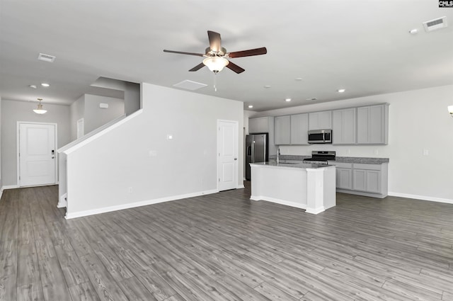 kitchen with wood finished floors, a center island with sink, a sink, appliances with stainless steel finishes, and open floor plan