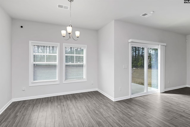 unfurnished dining area featuring dark wood-style floors, visible vents, baseboards, and a notable chandelier