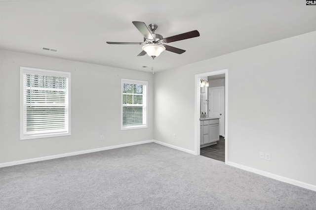 unfurnished bedroom with a ceiling fan, visible vents, baseboards, dark colored carpet, and connected bathroom