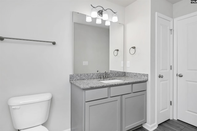 bathroom with baseboards, toilet, wood finished floors, and vanity