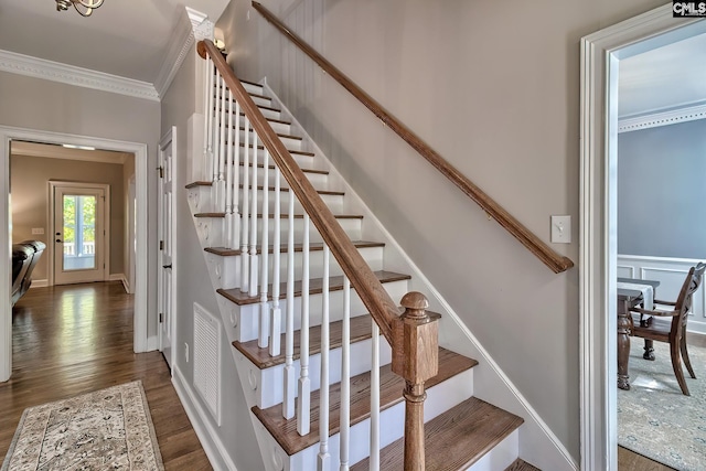 stairway with visible vents, wood finished floors, baseboards, and ornamental molding