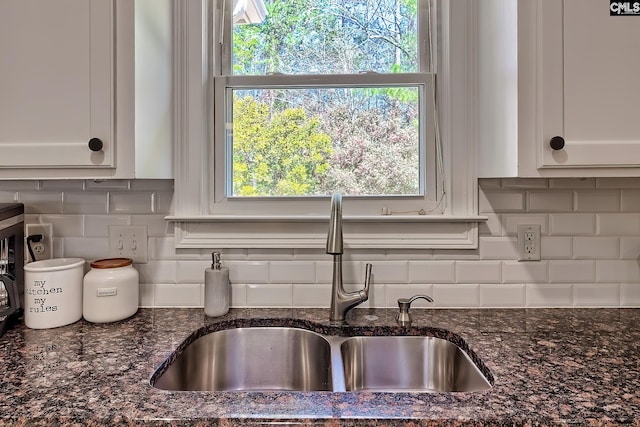 interior details with dark stone countertops, decorative backsplash, white cabinets, and a sink