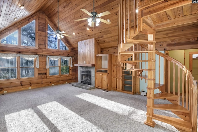 unfurnished living room featuring carpet, a tiled fireplace, stairway, wood walls, and wooden ceiling