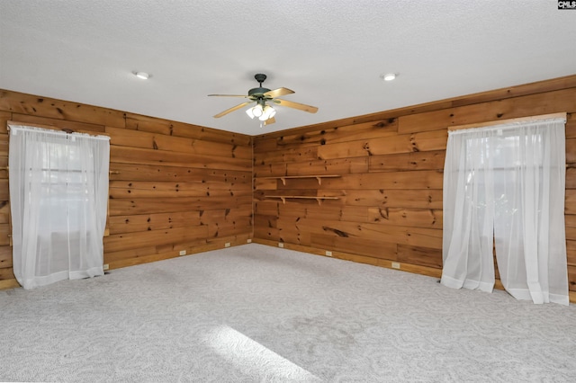 unfurnished room featuring wood walls, a textured ceiling, carpet, and ceiling fan