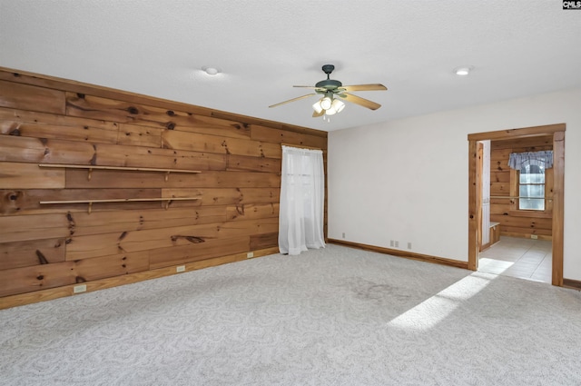 carpeted empty room with baseboards, wooden walls, and a ceiling fan