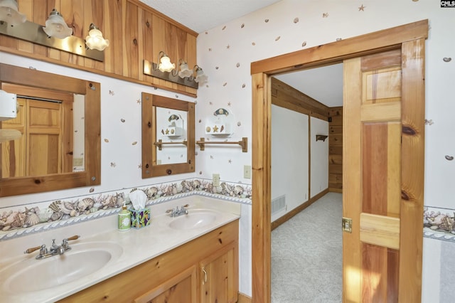 bathroom featuring double vanity, visible vents, wallpapered walls, and a sink