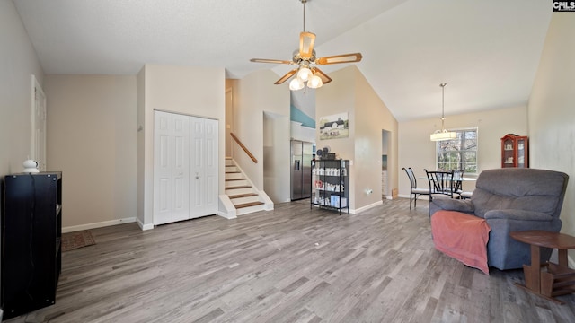 living area with ceiling fan, baseboards, stairway, wood finished floors, and high vaulted ceiling