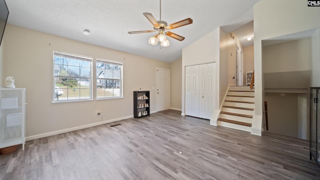 unfurnished living room with lofted ceiling, a textured ceiling, wood finished floors, and stairs