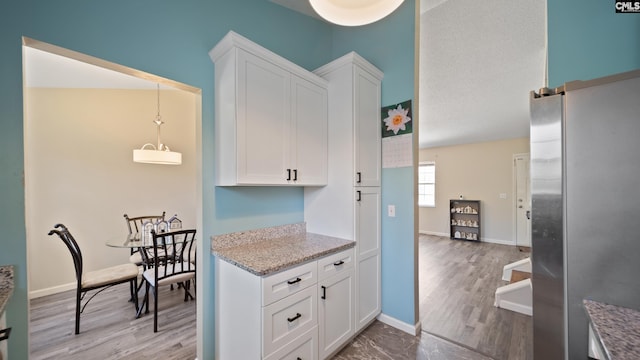 kitchen featuring light wood-type flooring, white cabinetry, freestanding refrigerator, and baseboards