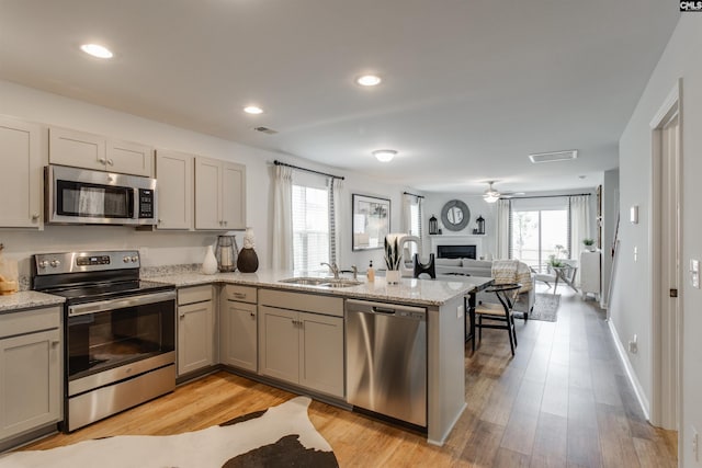 kitchen featuring a sink, open floor plan, appliances with stainless steel finishes, a peninsula, and a fireplace