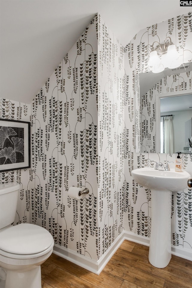 half bathroom with baseboards, toilet, wood finished floors, and vaulted ceiling