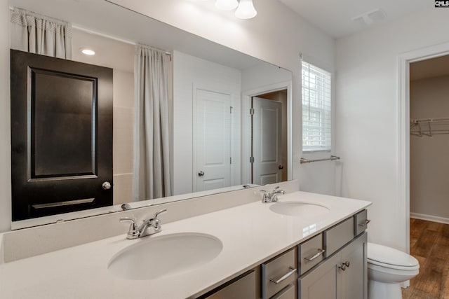 full bath featuring double vanity, toilet, wood finished floors, and a sink