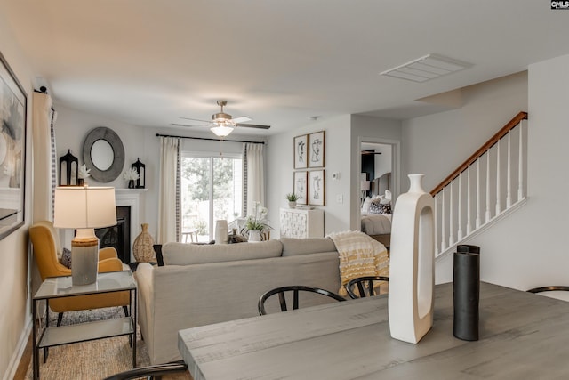 living room featuring visible vents, stairway, wood finished floors, a glass covered fireplace, and a ceiling fan