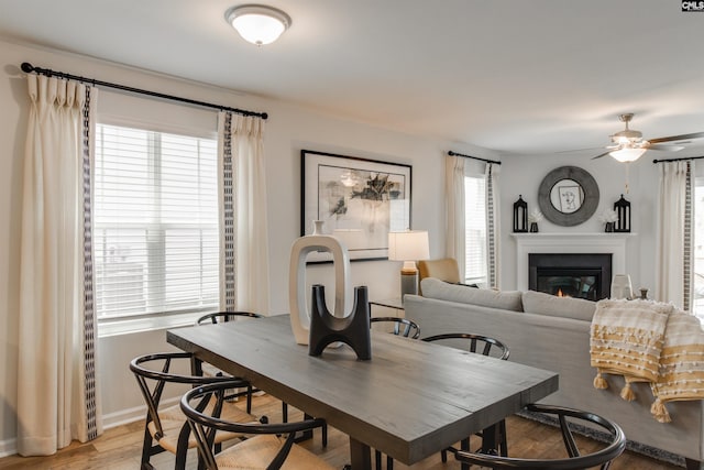 dining area featuring a glass covered fireplace, baseboards, light wood-type flooring, and a ceiling fan