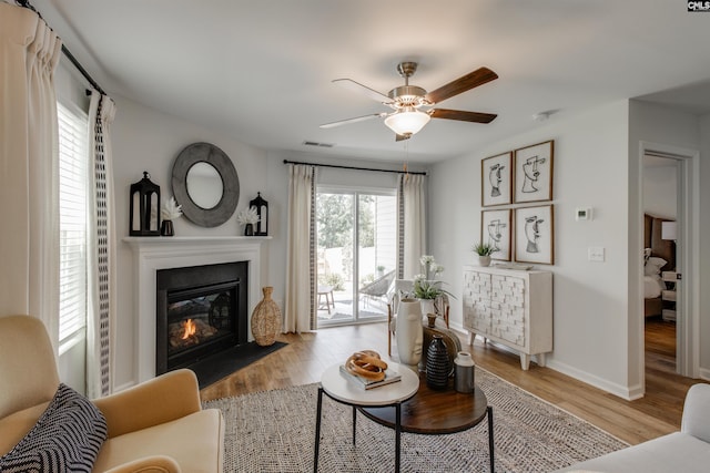 living area featuring visible vents, a fireplace with flush hearth, baseboards, and wood finished floors