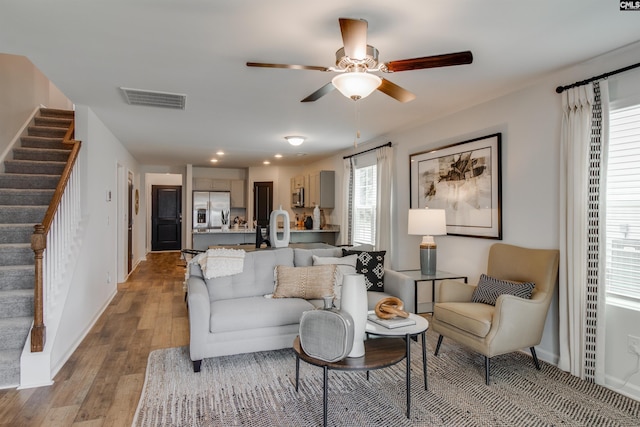 living room with light wood finished floors, visible vents, stairway, and ceiling fan