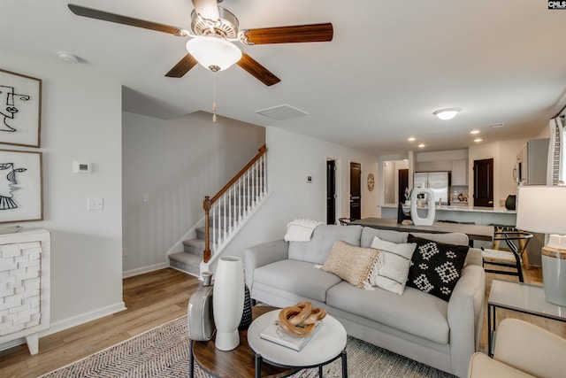 living room featuring light wood finished floors, visible vents, ceiling fan, baseboards, and stairway