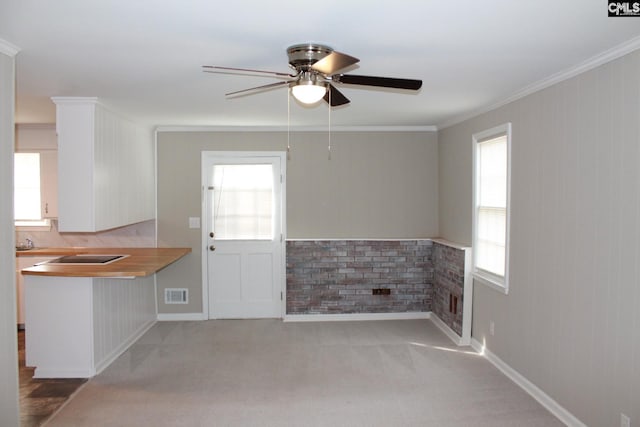 kitchen featuring visible vents, light colored carpet, ornamental molding, white cabinets, and a ceiling fan