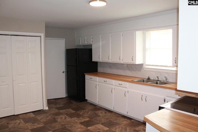 kitchen with a sink, wood counters, white cabinets, and freestanding refrigerator